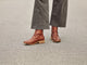 Woman wearing Hawk leather ankle boot in mahogany with gray pants