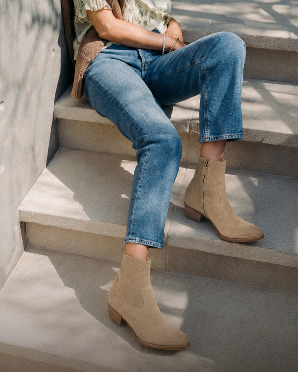 Woman wearing Cuervo suede boots in oat with jeans and blouse, sitting on steps