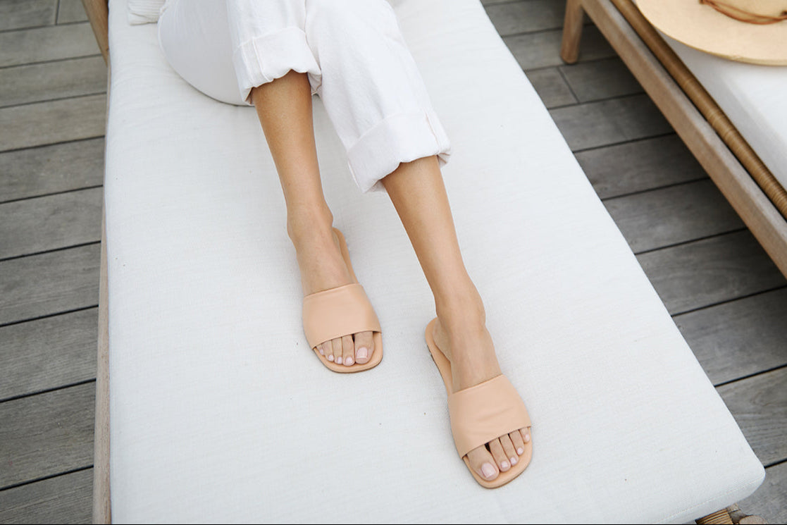 Woman wearing Honeybird leather slide sandals in beach with white pants and pink sweater