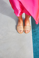 Woman wearing Hoopoe leather slide sandals in gold/honey with pink dress by the pool.