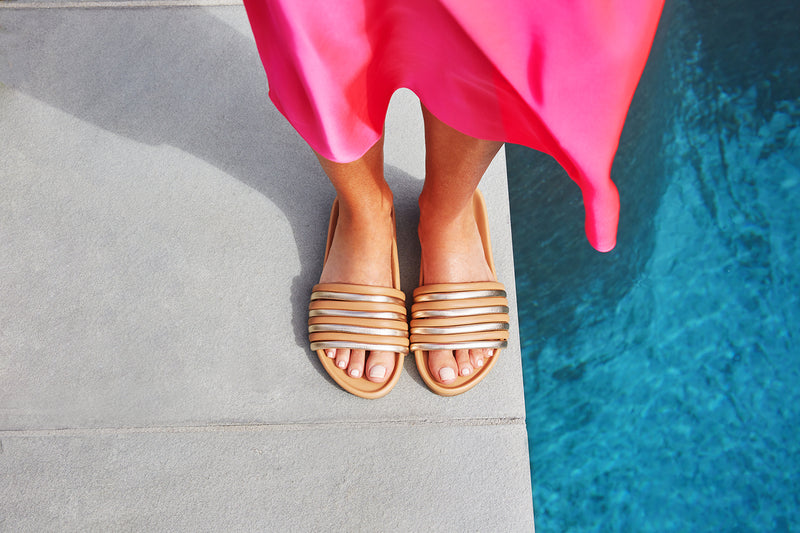 Woman wearing Hoopoe leather slide sandals in gold/honey with pink dress by the pool