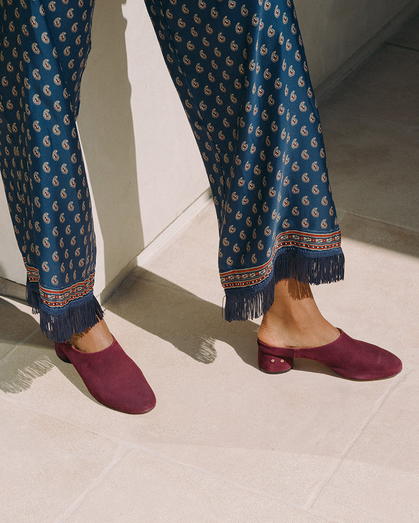 Woman wearing Jay suede heeled mules in prune with patterned pants