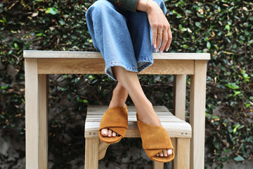 Woman wearing Kea suede slide sandals in caramel with jeans sitting on wooden table
