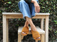 Woman wearing Kea suede slide sandals in caramel with jeans sitting on wooden table