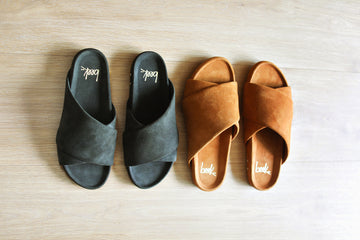 Group shot of Kea suede slide sandals in ivy and caramel on wood surface