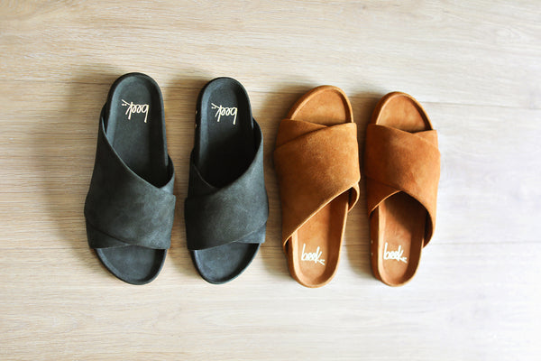 Group shot of Kea suede slide sandals in ivy and caramel on wood surface