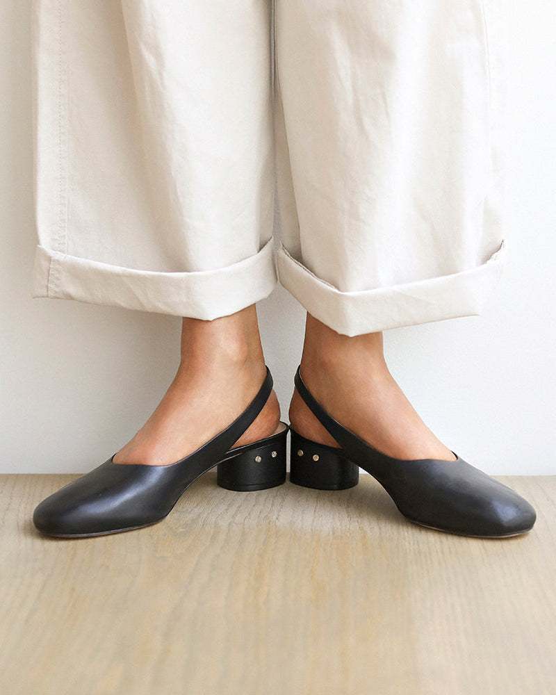Woman wearing Lora leather sling back heels in black with white pants