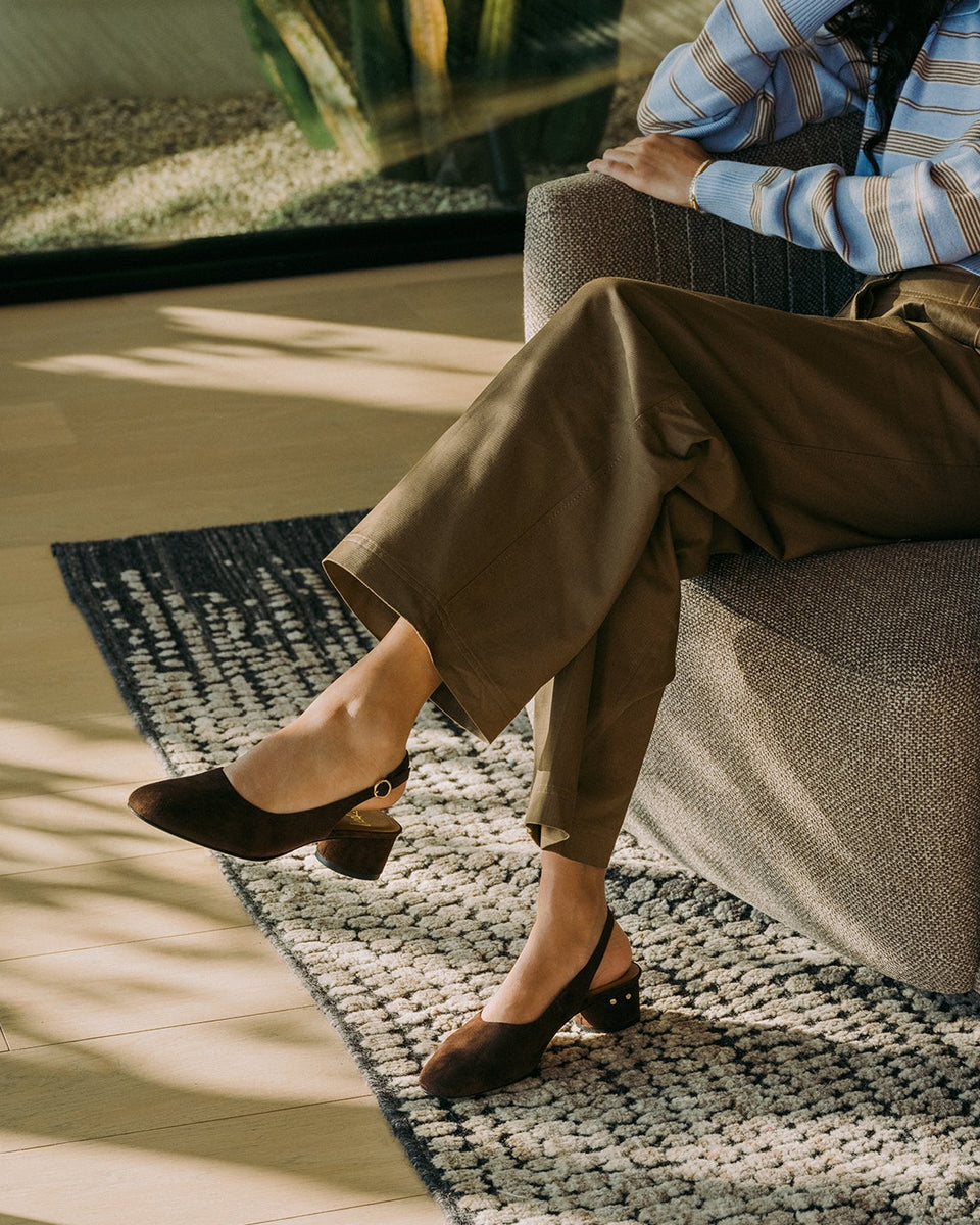 Woman wearing Lora suede heeled sling back shoes in chocolate with pants