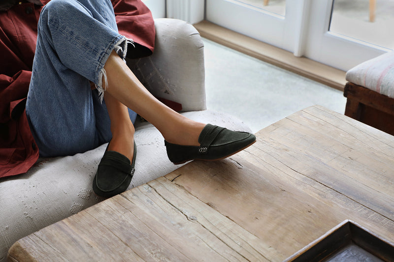 Woman wearing Moorhen suede loafers in ivy with jeans on couch