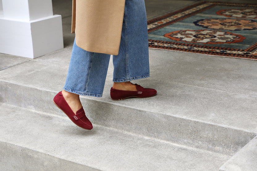 Woman wearing Moorhen suede loafers in port with jeans and long coat.