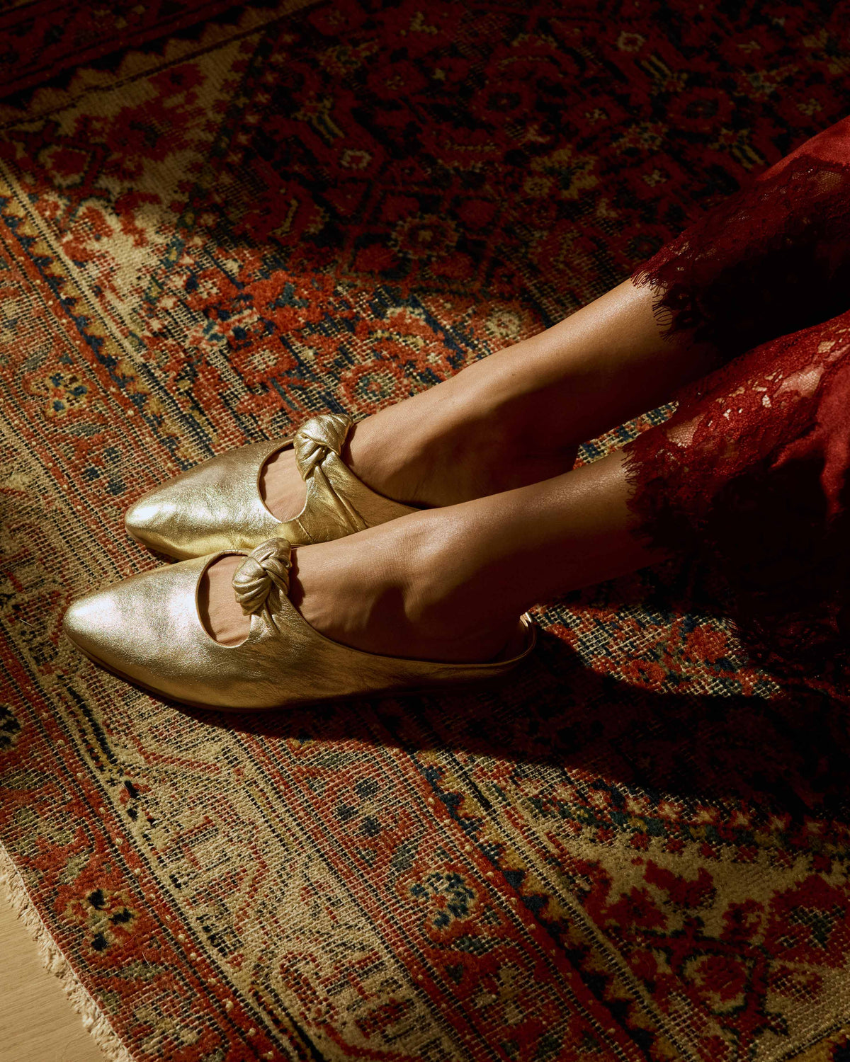 Woman wearing Noddy leather knotted mule in gold with red lace dress