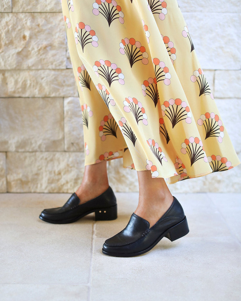 Woman wearing Owl leather heeled loafers in black with yellow patterned dress