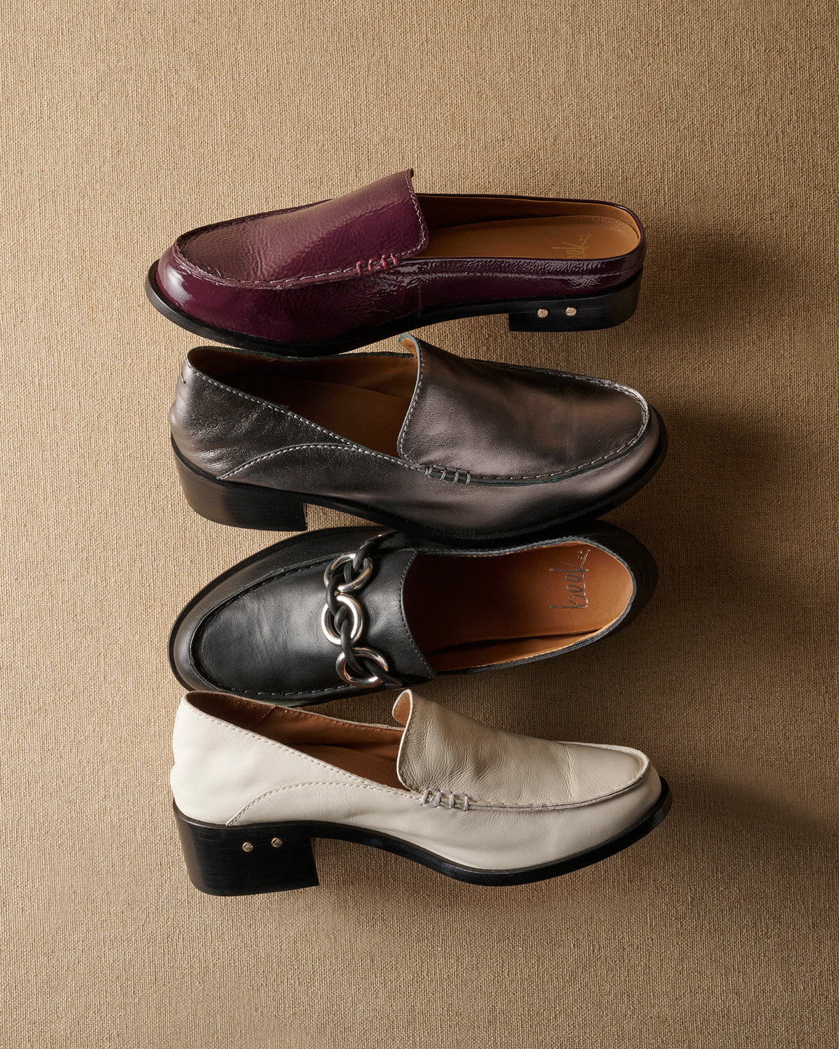 Group shot of Owlet backless loafer in patent leather prune, Owl leather loafer in gunmetal and eggshell, and Prion leather loafer in black
