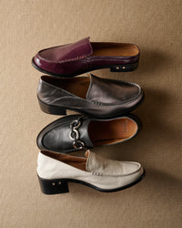 Group shot of Owlet backless loafer in patent leather prune, Owl leather loafer in gunmetal and eggshell, and Prion leather loafer in black