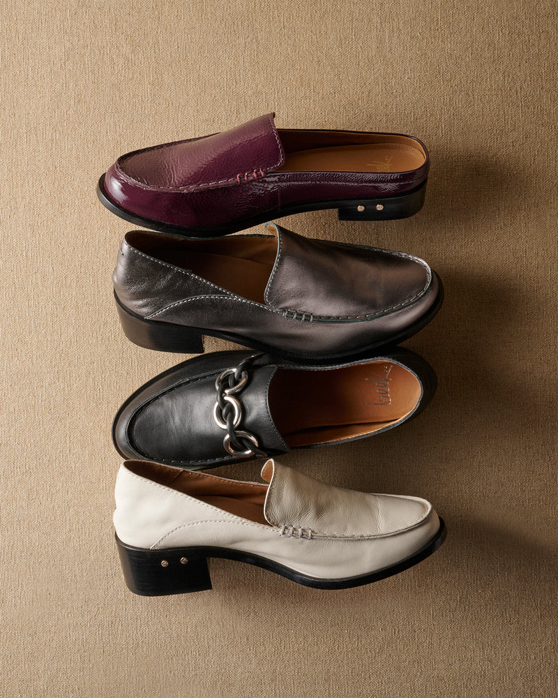 Group shot of Owlet backless loafer in patent leather prune, Owl leather loafer in gunmetal and eggshell, and Prion leather loafer in black