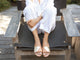 Woman wearing Paloma leather slide sandal in gold/honey with white pants and shirt
