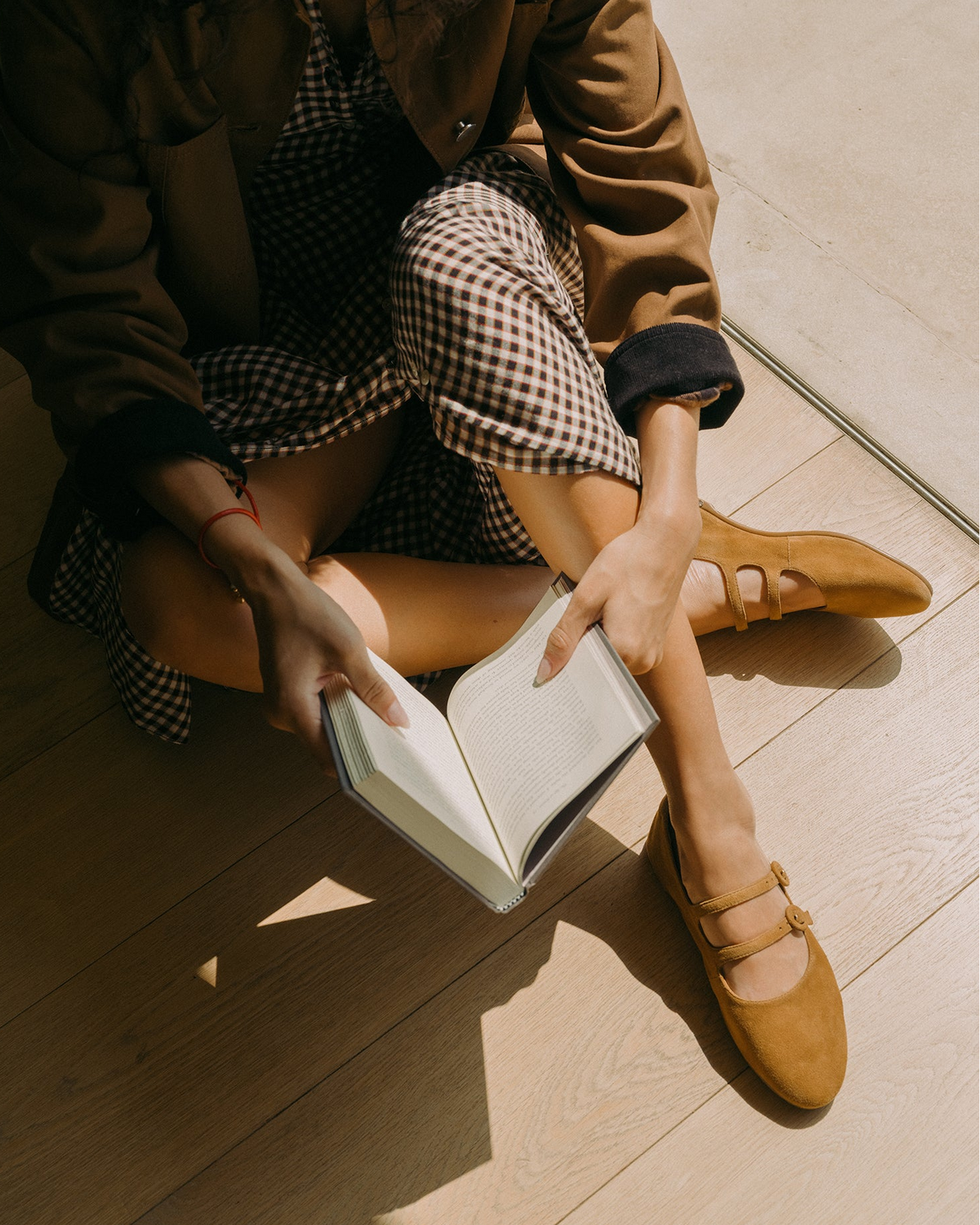 Woman wearing Partridge suede mary jane ballet shoes in toffee with checkered dress and coat, reading a book
