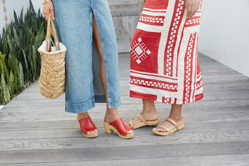 Woman wearing Peacock clogs in red with denim skirt next to woman wearing Dipper clogs in honey with red patterned skirt.
