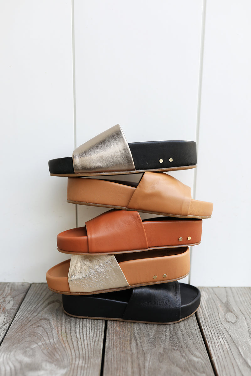 Group shot of Pelican leather platform sandals in bronze/black, honey, tan, gold/honey, and black (top to bottom).