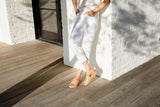Woman wearing Pelican leather sandals in honey with white pants and white top.