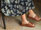 Woman wearing Pelican leather slide sandals in tan with floral dress sitting on stool