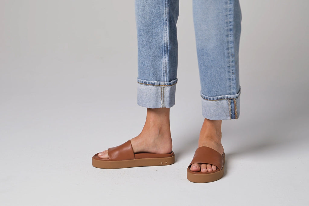 Video of woman walking in Chick leather slide sandals in tan wearing cuffed jeans