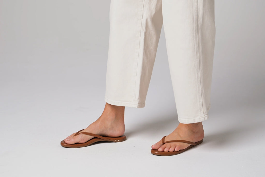 Video of woman walking in Sunbeam leather flip flop sandals in tan with white pants