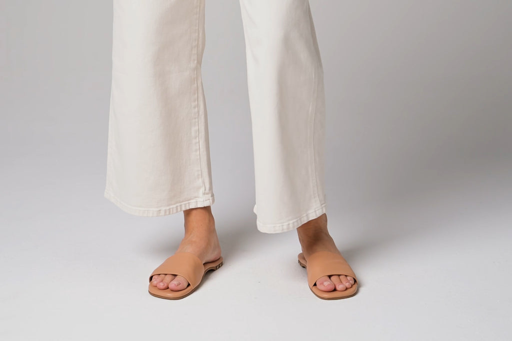 Video of woman walking in Honeybird leather slide sandals in beach with white pants.