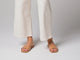 Video of woman walking in Honeybird leather slide sandals in beach with white pants.