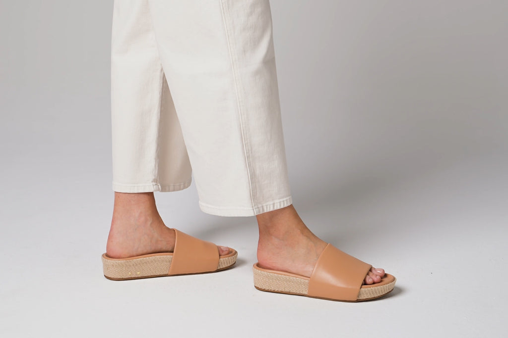 Woman wearing Pelican Jute leather platform sandals in beach with white pants