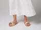 Woman walking in Tesia leather slide sandals in gold/beach with white dress