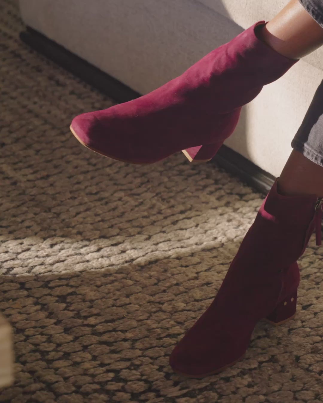 Video of woman wearing Raven suede square toe boots in prune with gray jeans, sitting on couch