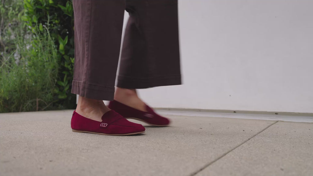 Woman wearing Moorhen suede loafers in port with dark jeans, walking.