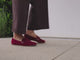Woman wearing Moorhen suede loafers in port with dark jeans, walking.