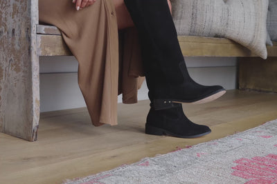 Video of woman wearing Nuthatch suede knee-high boot in black with tan shirt dress, sitting on bench and walking.