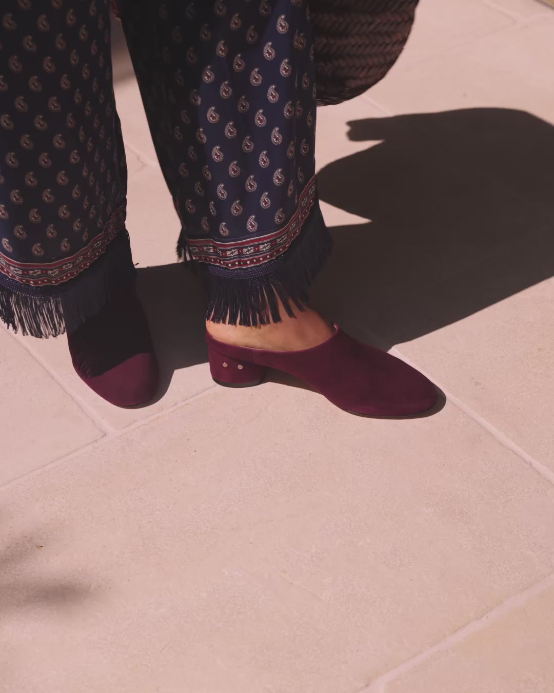 Video of woman wearing Jay suede heeled mules in prune with patterned pants, walking