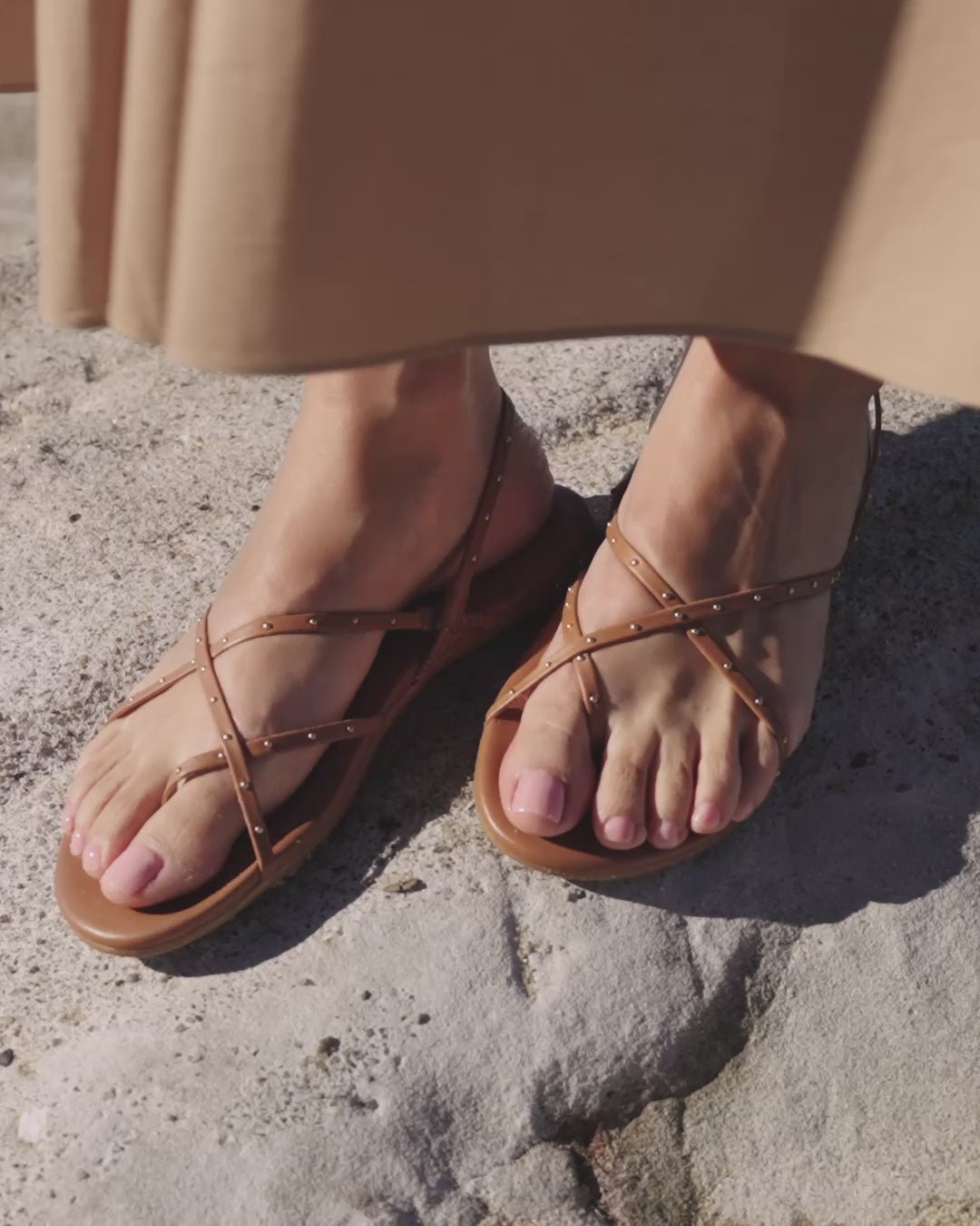 Video of woman wearing Palila leather sandals in tan with light tan dress standing on a rock