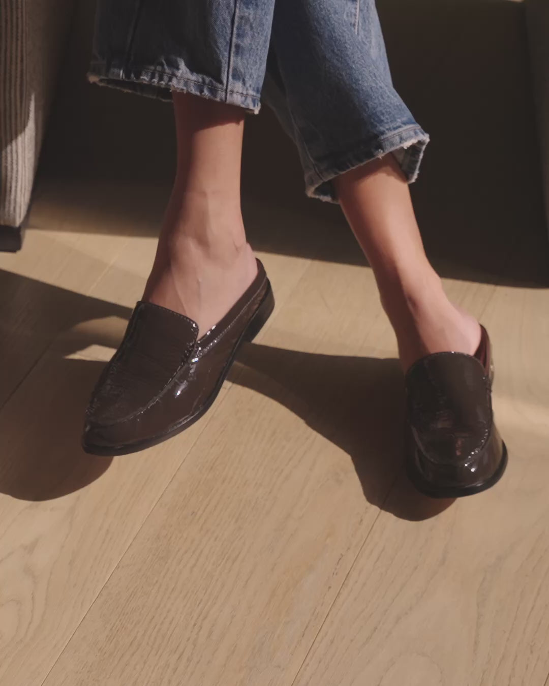 Video of woman wearing Owlet patent leather backless loafer mules in coffee with jeans, sitting