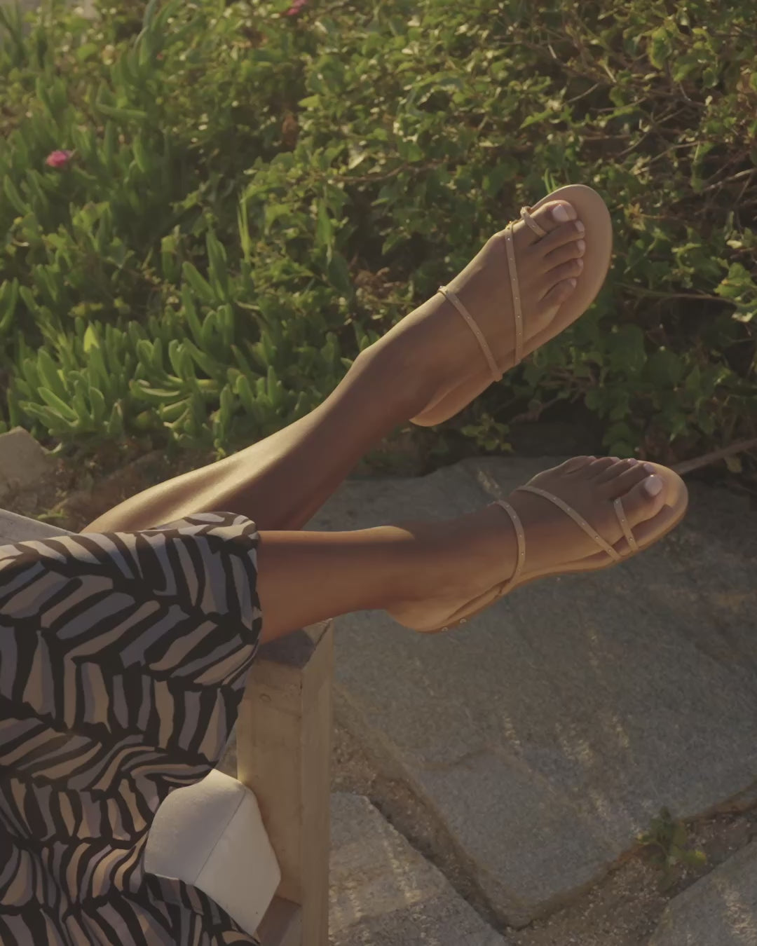 Video of woman wearing Ula leather sandals in beach with patterned dress sitting outdoors