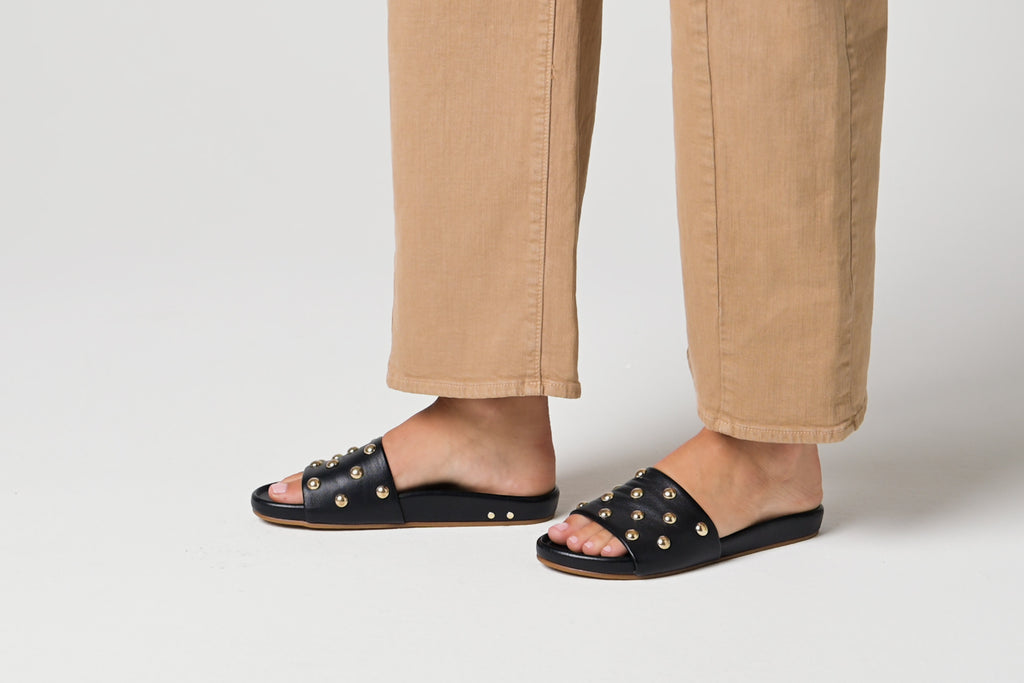 Video of woman walking in Gallito Stud leather slide sandals in black with tan pants