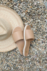 Puffbird Raffia slide sandals in beach next to hat.