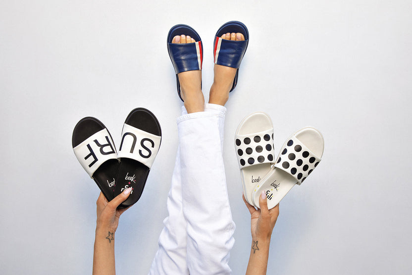 Woman wearing Railibird leather slide sandals in stripe while holding Railibird in surf and dot