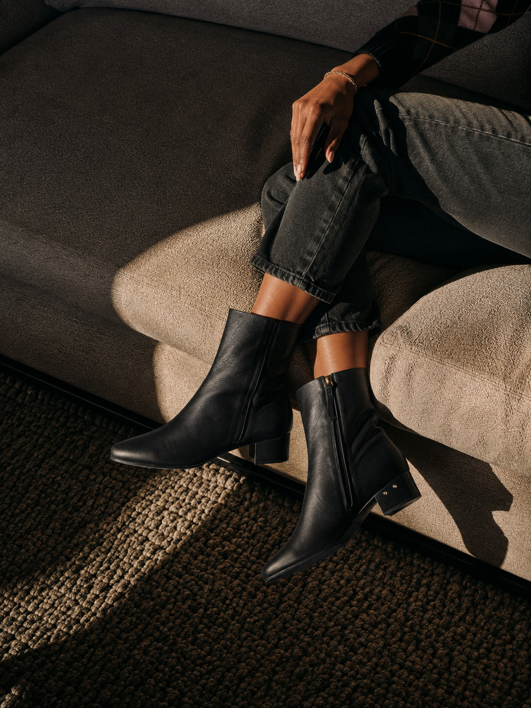 Woman wearing Raven boots in black leather with dark jeans, sitting on couch