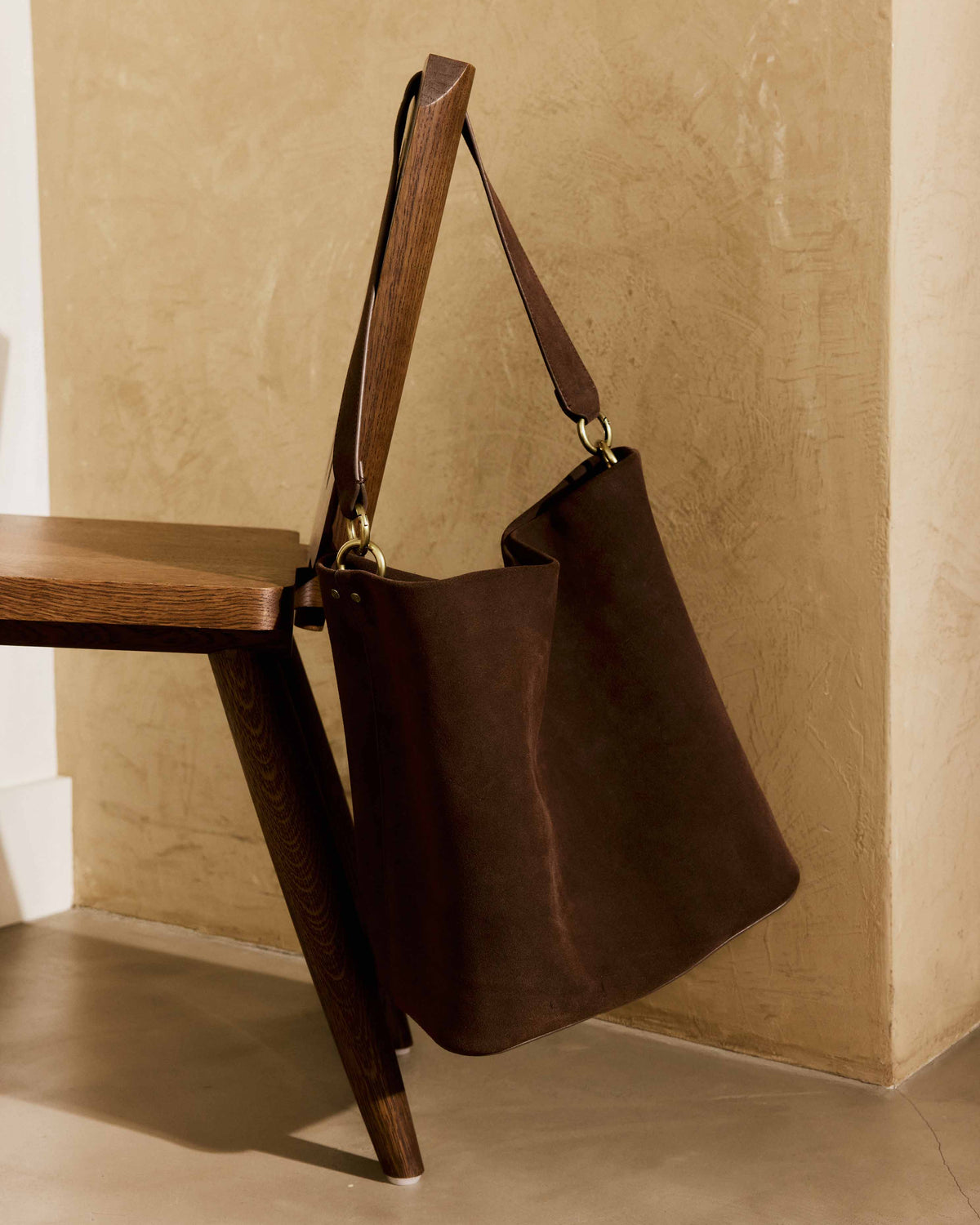 Sabine suede bucket bag in coffee hanging from a wooden chair