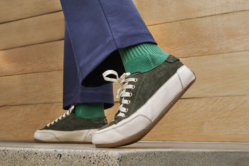 Model wearing Sandpiper suede sneaker shoes in ivy with green socks and blue pants