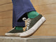 Model wearing Sandpiper suede sneaker shoes in ivy with green socks and blue pants