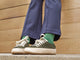 Model wearing Sandpiper suede sneaker shoes in ivy with green socks and blue pants