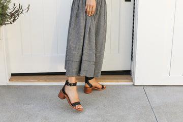 Woman wearing Sapphire leather ankle strap sandals in black with checkered dress
