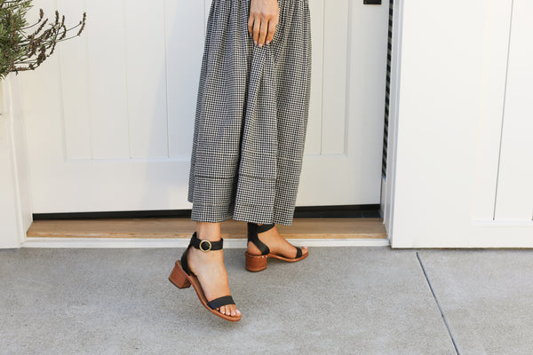 Woman wearing Sapphire leather ankle strap sandals in black with checkered dress