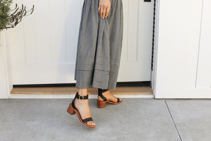 Woman wearing Sapphire leather ankle strap sandals in black with checkered dress